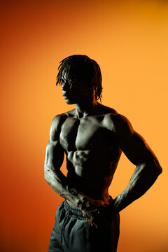 Muscular African man posing shirtless against orange backdrop