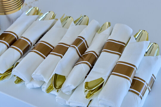 Elegant catering cutlery sets wrapped in white napkins with gold bands.