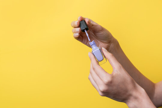 Caucasian woman hands holding nail polish on yellow