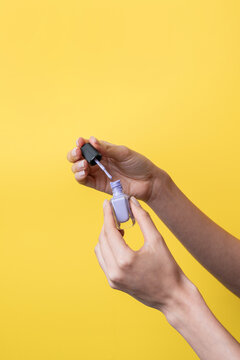 Caucasian woman hand holding nail polish on yellow background