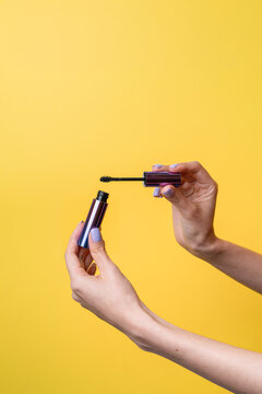 Caucasian woman hands holding mascara on yellow background