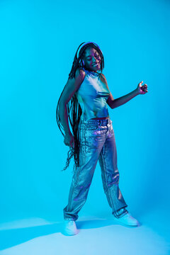 Joyful afro woman dancer wearing headphones in neon studio