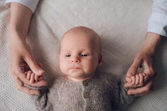 Newborn baby holding parent hands on cozy bed at home