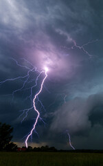Vertical view of a powerful lightning strike bolts flashing down to the ground during a severe night thunderstorm © FotoBastek