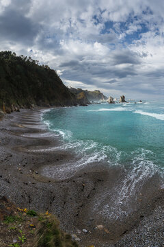 Asturian rocky coast with turquoise waves under stormy sky