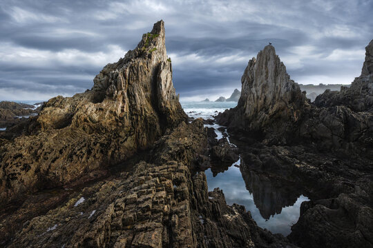 Dramatic Asturian sea stacks and tide pool under stormy sky