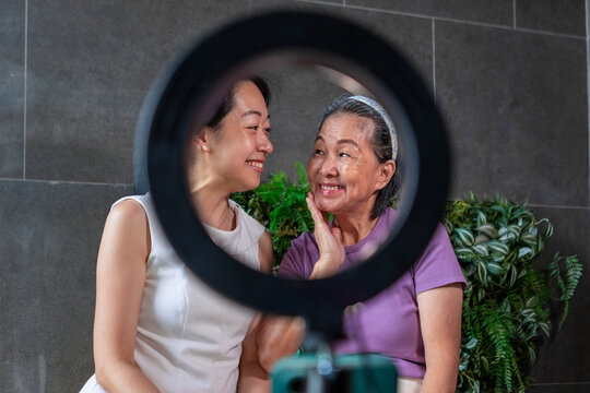Smiling mother and daughter filmed with ring light indoors
