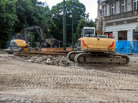 A tracked and wheeled excavator operating at a demolition site. Urban redevelopment, tearing up old concrete. The machinery is engaged in groundworks, clearing site debris. engaged in breaking up. 