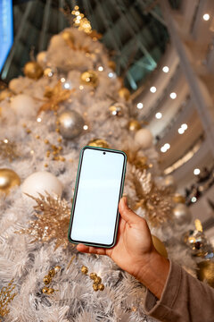 Smartphone with blank screen by festive Christmas tree