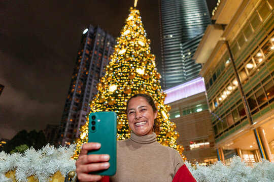 Woman taking selfie by Christmas tree in Malaysia at night