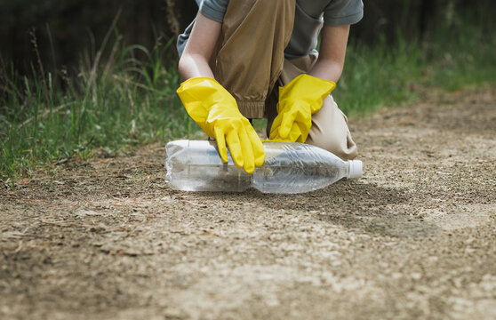 Person picking up plastic bottle litter on forest path