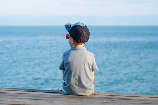 Child sitting on wooden pier looking out at sea