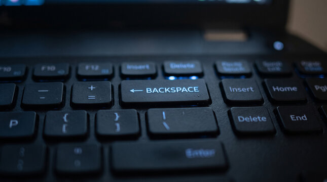 Close-up of a dark laptop keyboard with illuminated keys, emphasizing the backspace and enter buttons. The image captures the essence of digital interaction and technology