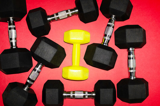 Dumbbells on red background with single yellow standout