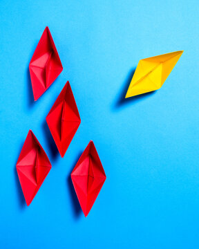 Yellow Paper Boat Moving Away From Red Paper Boats On Blue Background