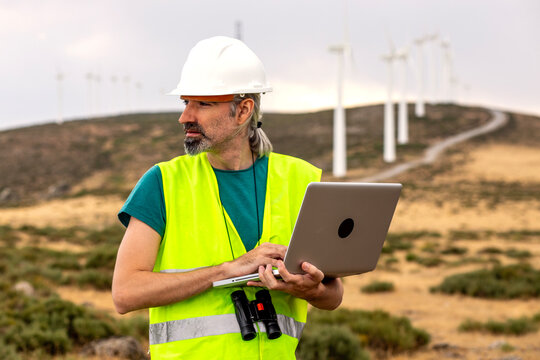 Wind farm technician checking turbine status with laptop