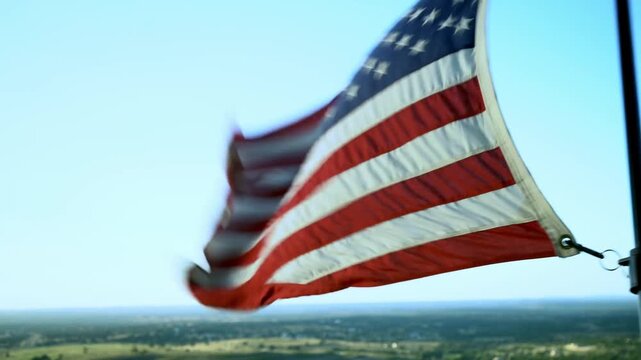 Large Red White and Blue American Flag Blowing in the Wind From Side of Tall Building Overlooking Rolling Green Hills With Blue Sunset Sky