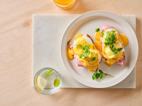 Egg benedict brunch on a white plate with drinks