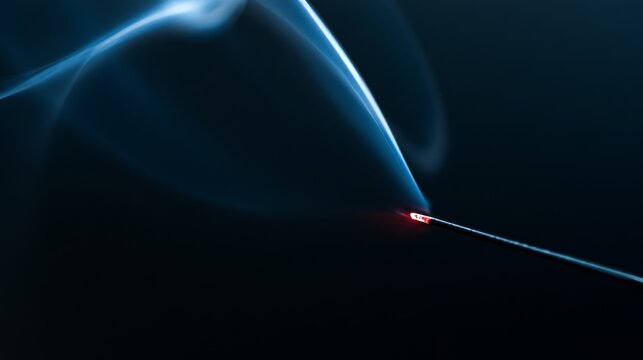 Burning incense stick with glowing ember releasing delicate smoke on black background, creating peaceful meditation atmosphere with elegant curves, spiritual ritual concept and calming relaxation mood