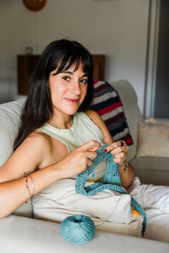 Woman knitting with blue yarn while relaxing on sofa