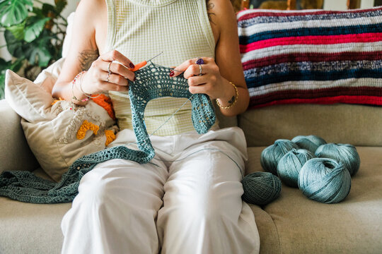 Woman crocheting at home with blue yarn on sofa