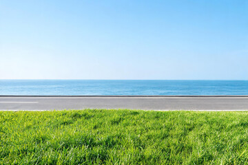 Obraz premium A straight asphalt road runs between lush green grass and a calm blue sea under a clear bright sky.