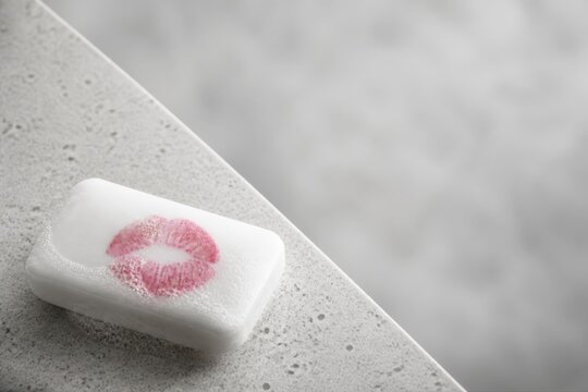 White soap bar with pink lipstick kiss on textured stone background