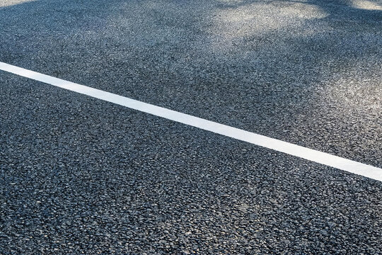 A close-up view of a dark asphalt road surface with a straight white traffic line marking, showing fine aggregate texture.