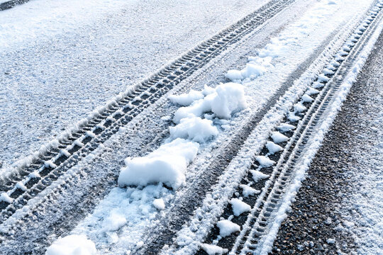 Snow lies on an asphalt road marked with distinct vehicle tire tracks in winter.