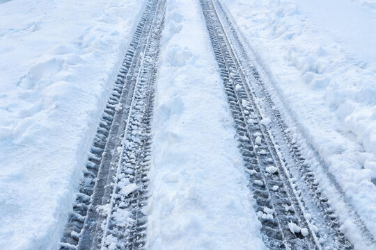 Two parallel tire tracks cut through fresh white snow on a wintry outdoor path, showing vehicle movement.