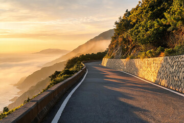 Obraz premium A winding mountain road cuts through coastal terrain at sunrise, with mist drifting over distant peaks and warm golden light illuminating the landscape.