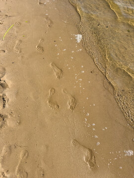 Footprints and tire tracks in wet sand on river beach, human trace concept