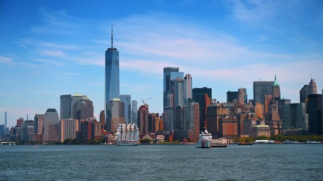 Tall ship and Coast Guard cutter near Lower Manhattan skyline. Full sails catch the wind as One World Trade Center rises behind calm harbor water.