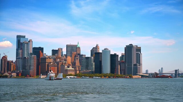 Lower Manhattan skyline with Coast Guard cutter. A white patrol ship and sailboat cross blue water beneath scattered clouds on Independence Day.