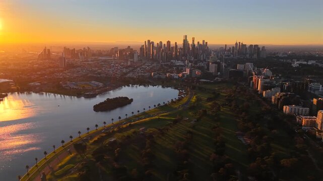 Aerial drone video at sunset over Albert Park, showing Albert Park Lake, Albert Park Golf Course, South Melbourne, Southbank and the Melbourne CBD skyline