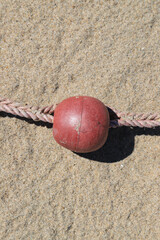 Close-up of Red Plastic Fishing Float with Rope on Sandy Beach © Lijuan