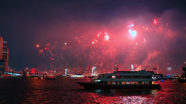 Cruise boat under red Independence Day fireworks in New York. Red smoke glows across the night sky and water as passengers gather on the upper deck.