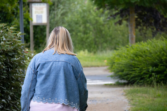 Blonde woman walking through green park wearing denim jacket