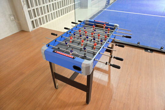 high-angle view of a blue foosball table positioned on a wooden floor near a glass partition wall.