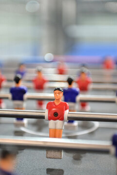 shallow depth of field shot highlighting a red foosball figurine on a rod with blurred players in the background. vertical orientation