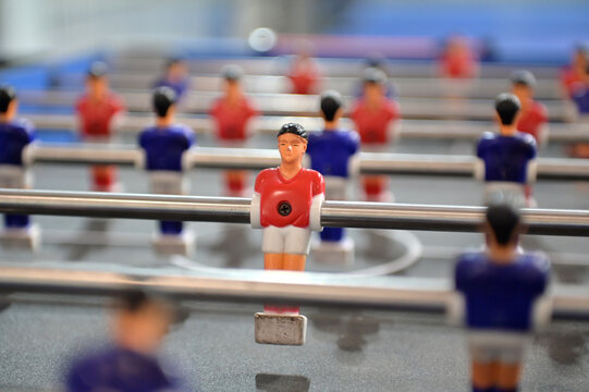 shallow depth of field shot highlighting a red foosball figurine on a rod with blurred players in the background. horizontal orientation