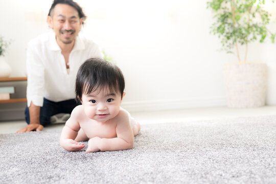 ハイハイする赤ちゃんを見守る父親 育児・子育て・成長・親子のふれあいのイクメン育休パパと赤ちゃんのイメージ