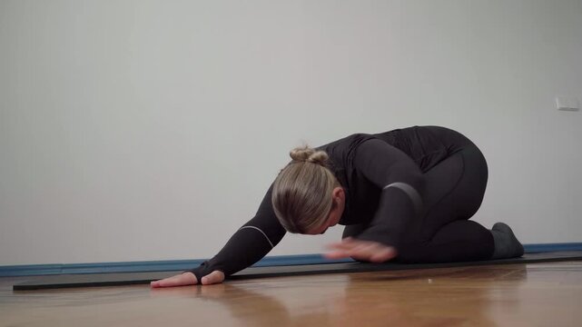 Woman in black sportswear holds child&rsquo;s pose on a mat, stretching her spine and hips for lower back pain relief and recovery.