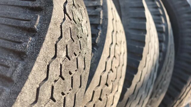 Detailed macro slow motion focus on the worn rubber tread patterns of several old heavy truck tires stacked outdoors.
