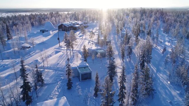 Aerial view of glass igloo resort in snowy lapland forest during sunny winter day.