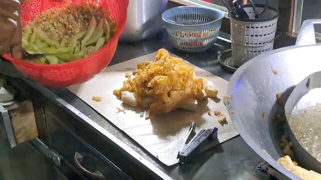 Indonesian street vendor making Tahu Tek Telur. Process includes whisking egg, frying omelette and tofu, cutting lontong with scissors, and making peanut petis sauce. Authentic Surabaya street food.