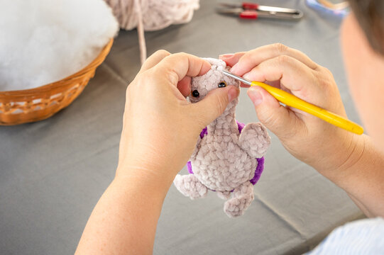 Hands of craftswoman stitching soft plush turtle head using crochet hook. Detailed view of creating handmade amigurumi toy during craft masterclass tutorial