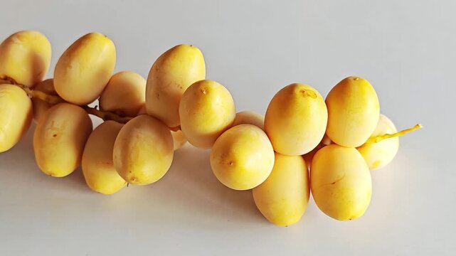 Single Fresh Yellow Date Palm Branch on White Surface.