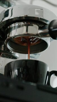 4K Pouring coffee stream from professional machine in cup. Barista man making double espresso, using filter holder. Flowing fresh ground coffee. Drinking roasted black coffee in the morning.