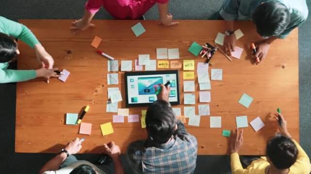 Top down view of programmer brainstorming and planning about web design while looking at tablet wireframe prototype. Aerial view of skilled developer team talking about digital application. Symposium.